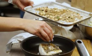 Image of Muscle Gain Fit Food Class participant sprinkling toasted macadamia nuts on cod