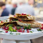 Plate with stacked stuffed flatbreads garnished with pomegranate seeds and fresh herbs, close-up