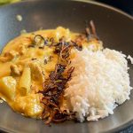 Creamy yellow curry with chunks of chicken and potatoes served with white rice and crispy fried onions on top in a bowl.
